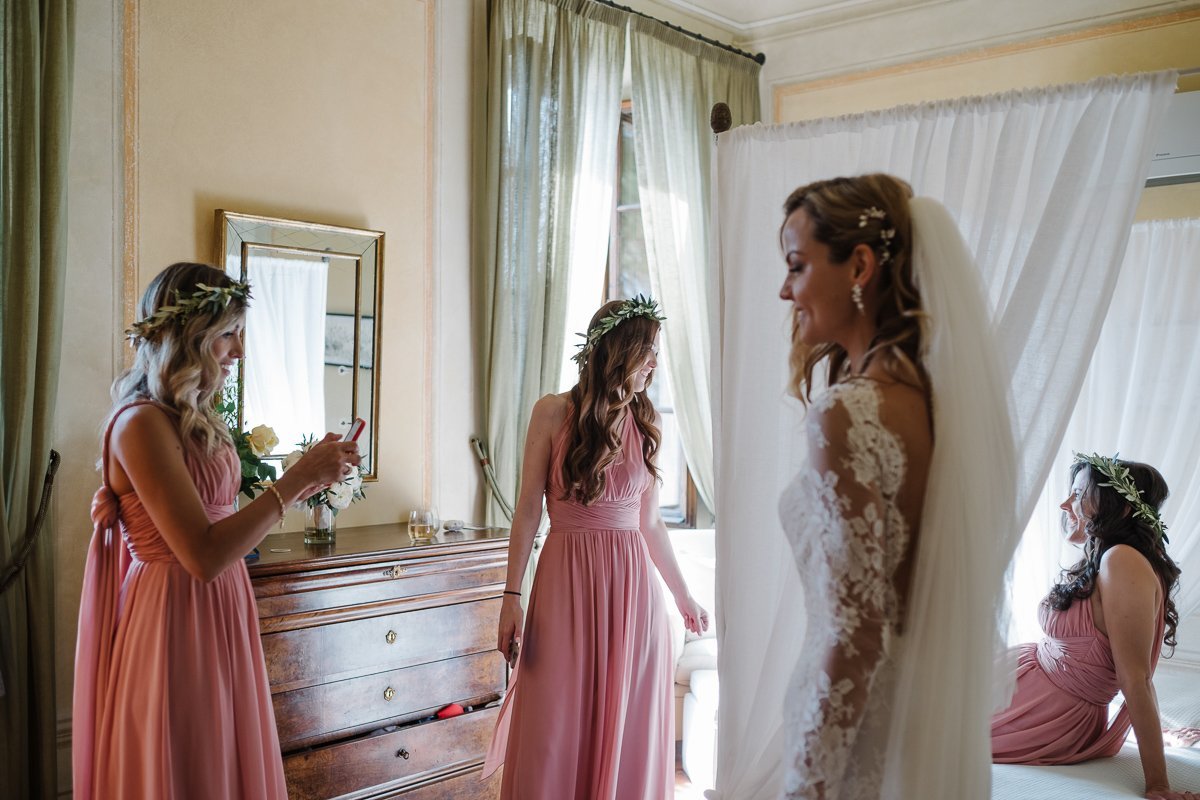 Bridesmaids in pink helping the bride into her dress