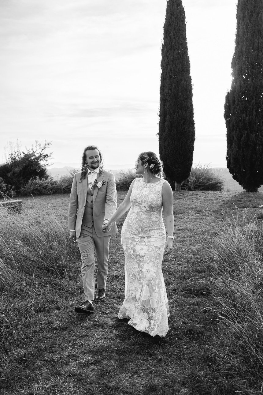 Bride and groom walking hand in hand among cypress trees in Tuscany
