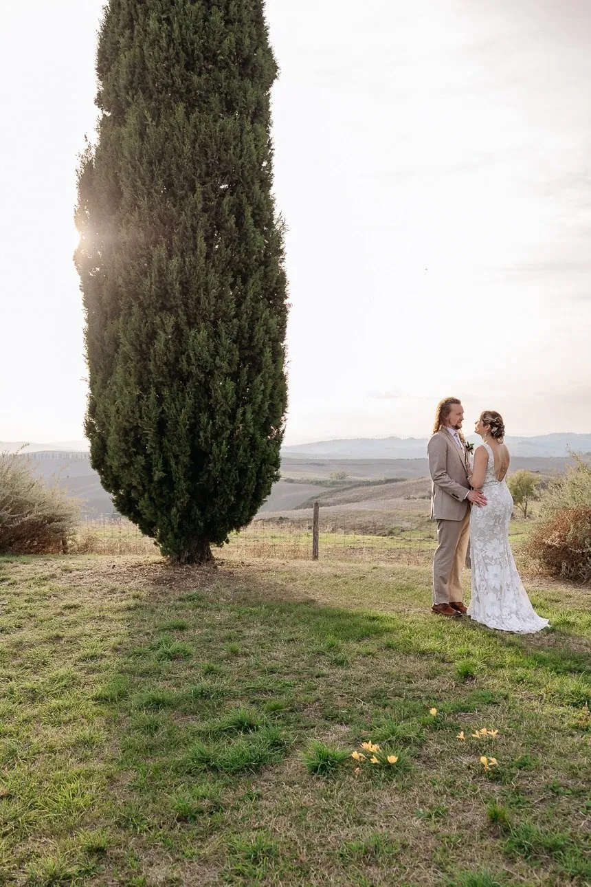 Bride and groom next to a cypress at sunset near Montalcino