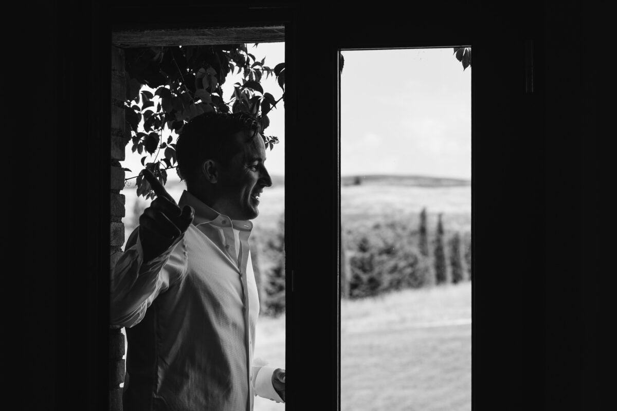 Groom framed in a doorway with the Val d'Orcia hills behind, black and white