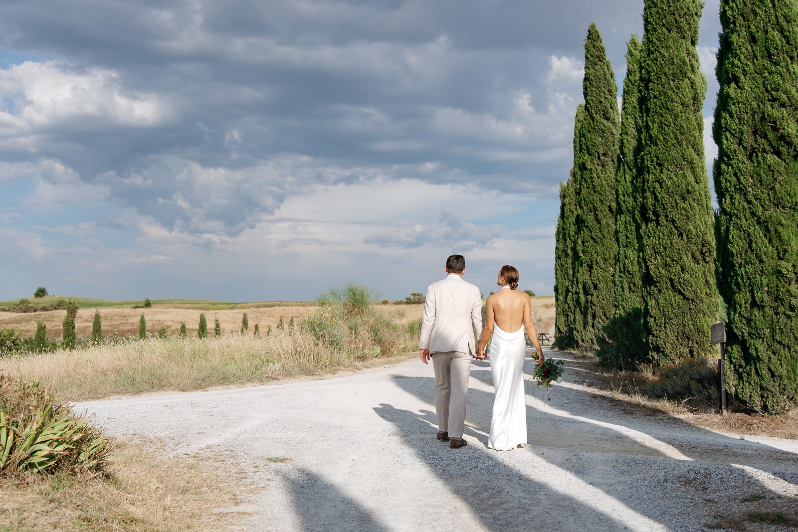Bride and groom walking down the cypress-lined drive at Il Rigo